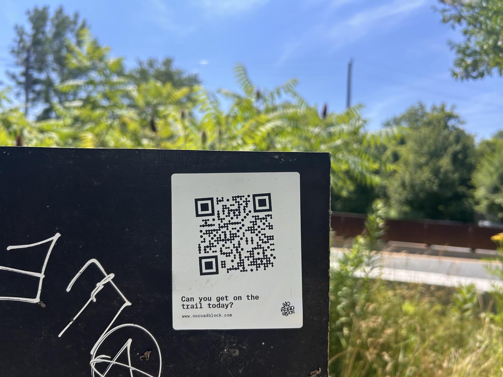Close-up of a No Road Block sticker on a black trailhead board asking 'Can you get on the trail today?' with a black QR code