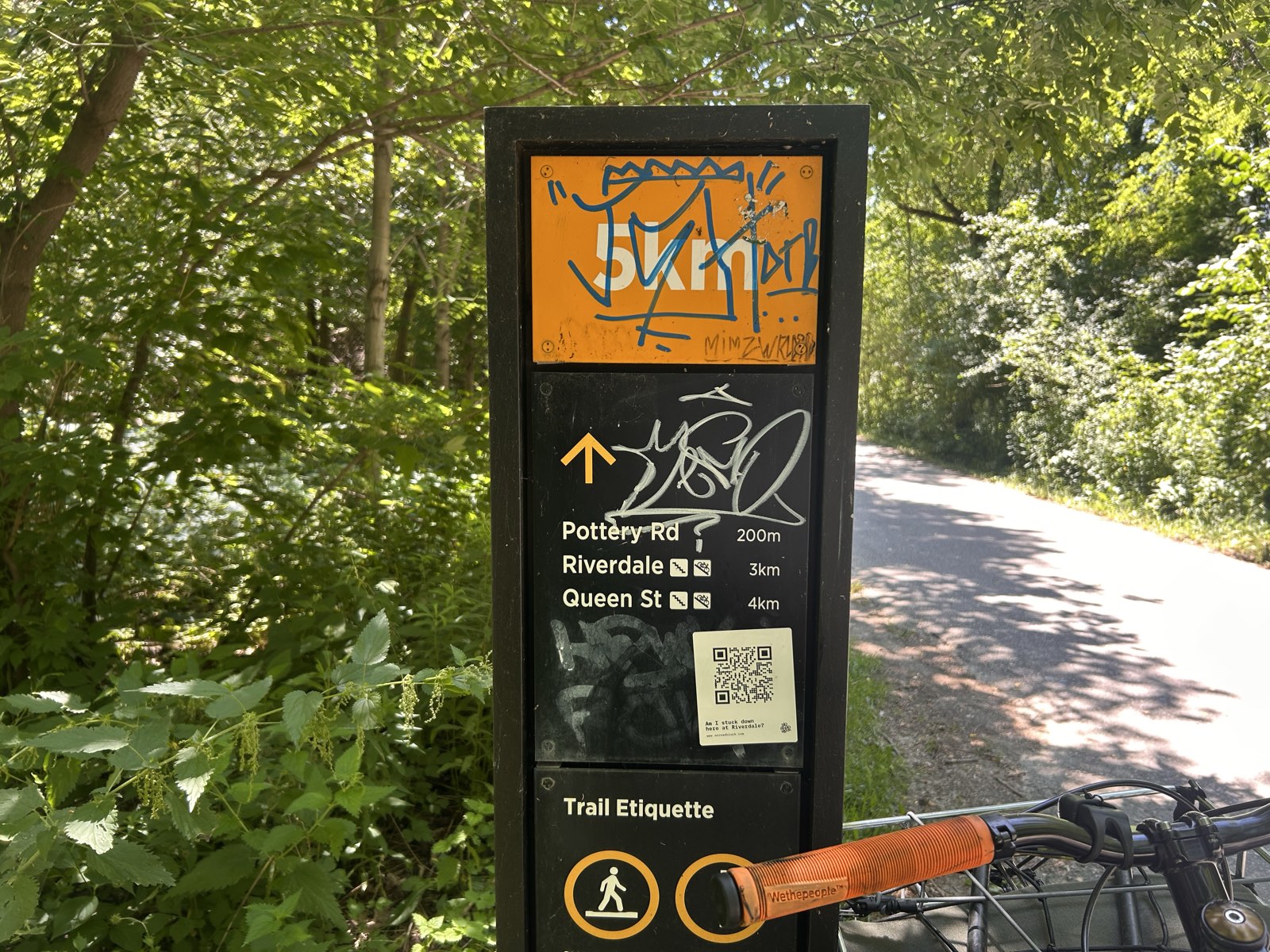 No Road Block sticker on a trail wayfinding pillar listing Pottery Rd 200 m, Riverdale 3 km and Queen St 4 km